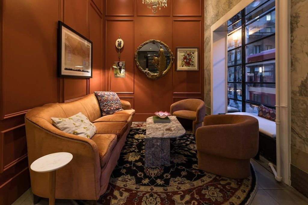 Een sfeervolle lounge met oranje fauteuils, een bank en een rond spiegeltje tegen een terracotta gelambriseerde wand