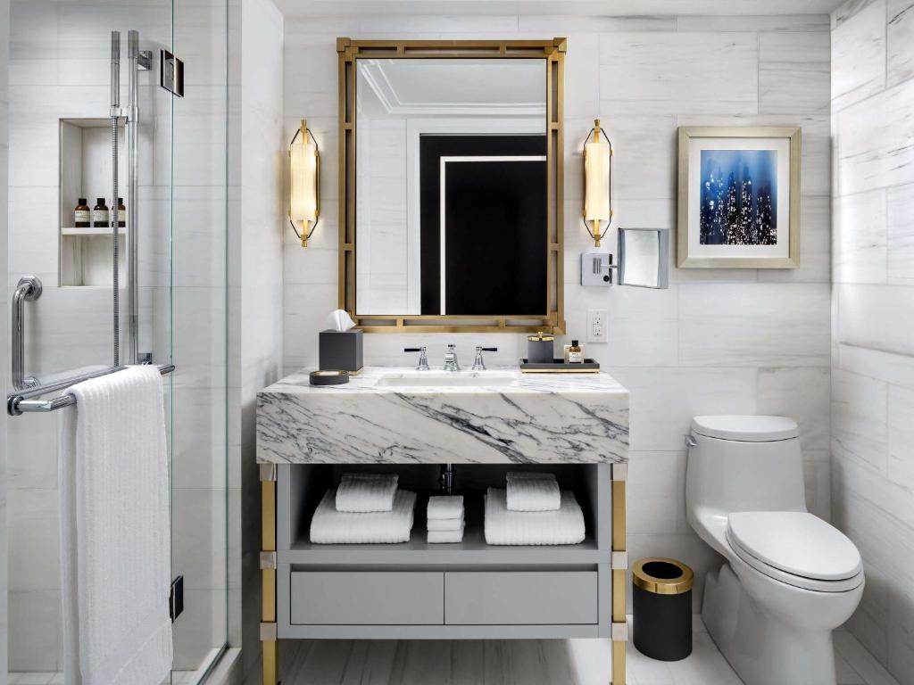 Badkamer met een marmeren wastafelblad, gouden armaturen en opgevouwen witte handdoeken op een plank