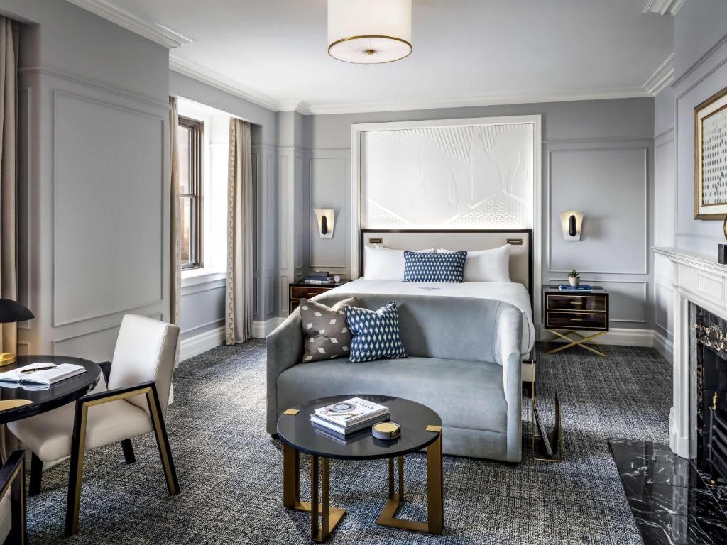 Grijze hotelkamer met een tweepersoonsbed, een lichtblauwe bank en een ronde salontafel, ingericht in een moderne stijl