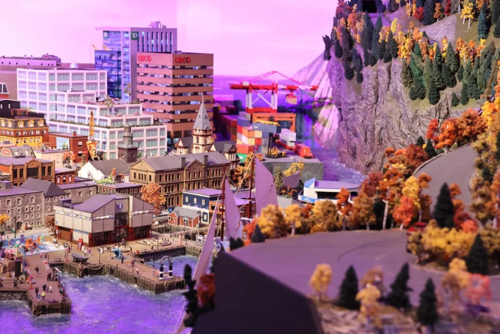 Gedetailleerd schaalmodel van een havenstad met gebouwen, een kraan en herfstkleurige bergen, gefotografeerd onder paars licht