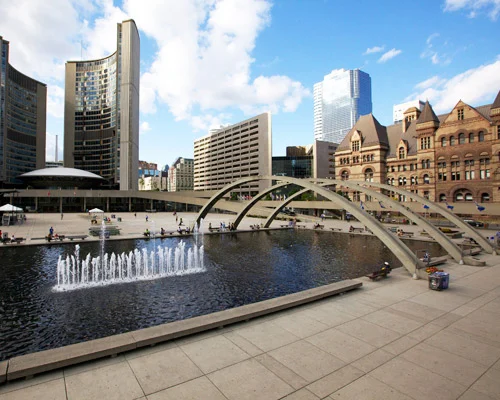 Plein met fonteinen en een boogbrug voor het gebogen stadhuis van Toronto, met wolkenkrabbers op de achtergrond onder een blauwe lucht