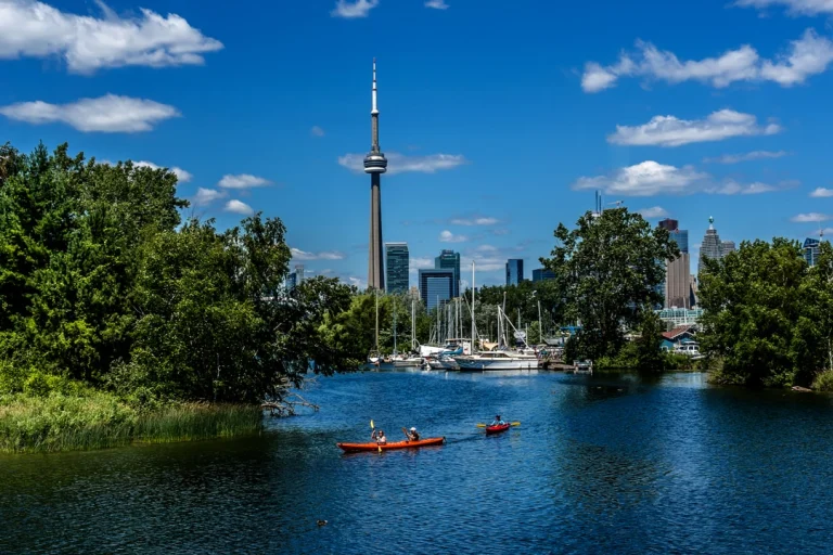 Rond bloemperk met rode bloemen in een park met gemaaid gras en herfstbomen, met water op de achtergrond in Toronto
