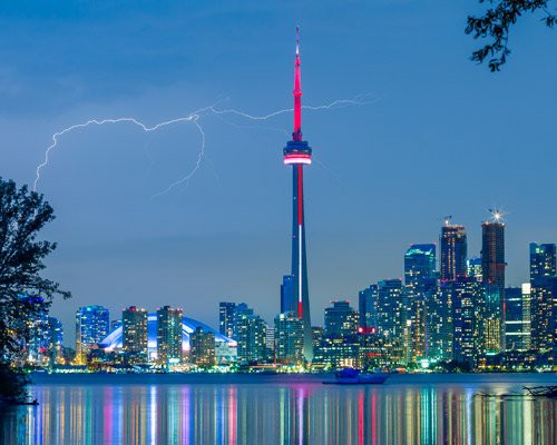 Bliksemschichten boven de verlichte CN Tower en de skyline van Toronto weerspiegeld in het water bij avondschemering