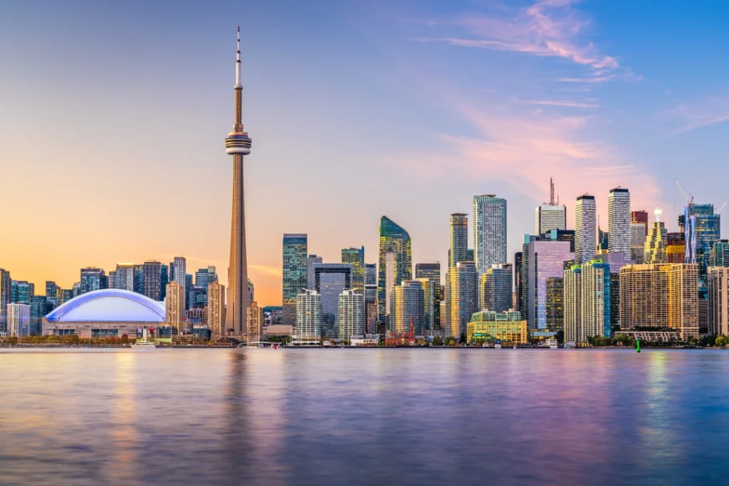 De CN Tower en wolkenkrabbers van Toronto tegen een roze en oranje avondlucht, gezien over het water met het Rogers Centre op de voorgrond