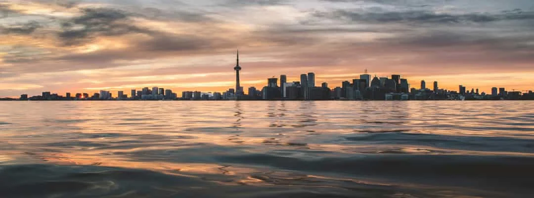 De skyline van Toronto met de CN Tower silhouetteert tegen een oranje avondlucht, gezien vanaf het water