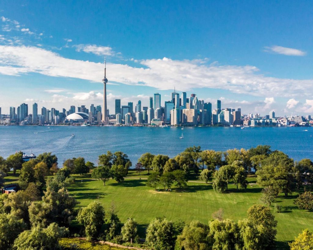 Groen park met bomen op de voorgrond en de skyline van Toronto met de CN Tower over het water gezien vanaf de Toronto Islands