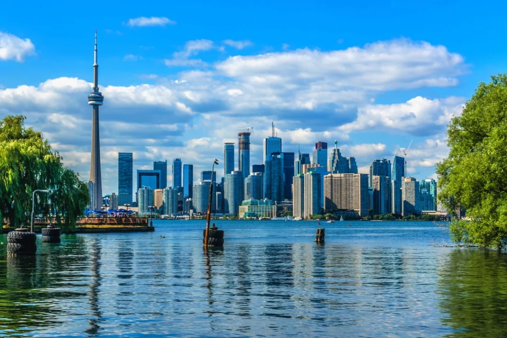 Uitzicht over het water op de skyline van Toronto met de CN Tower en wolkenkrabbers onder een blauwe hemel met wolken