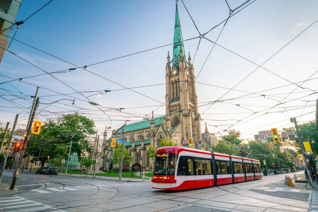 Rode en witte tram rijdt over een kruising in het centrum van Toronto met een hoge kerktoren en bovenleidingen op de achtergrond