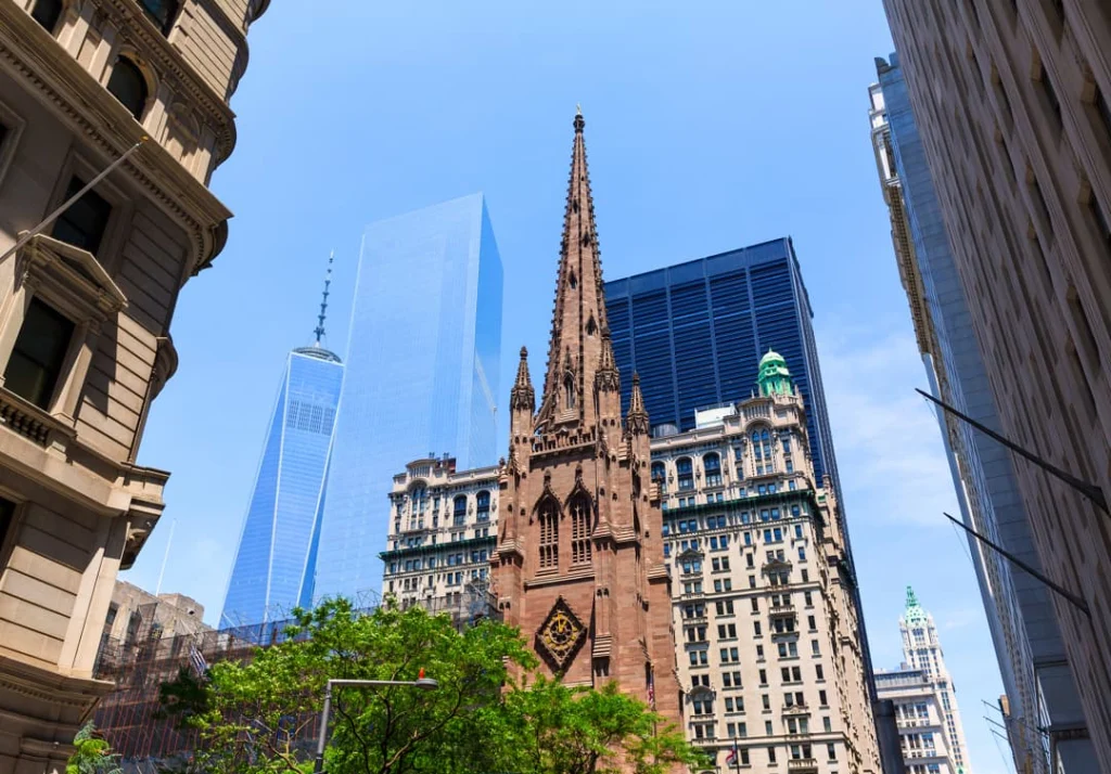 De torenspits van Trinity Church omringd door wolkenkrabbers in Lower Manhattan, waaronder One World Trade Center