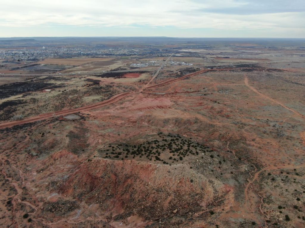 Luchtfoto van een rood aardlaagprofiel en een onverharde weg in de woestijn, met de rand van een stad aan de horizon bij Tucumcari in New Mexico