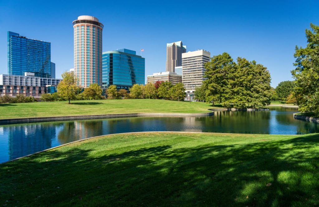 Grasveld met een vijver op de voorgrond en kantoortorens, waaronder een opvallende ronde toren, van het centrum van Tulsa op de achtergrond