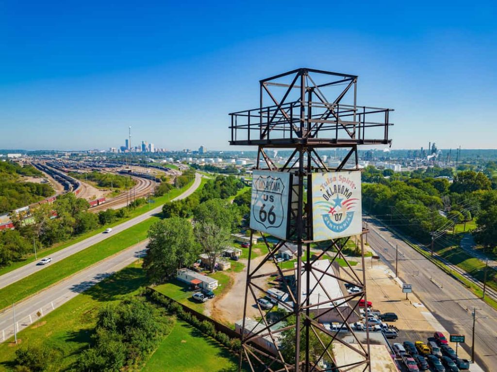 Metalen uitkijktoren met borden voor route 66 en het centennial van Oklahoma, met de skyline van Tulsa op de achtergrond