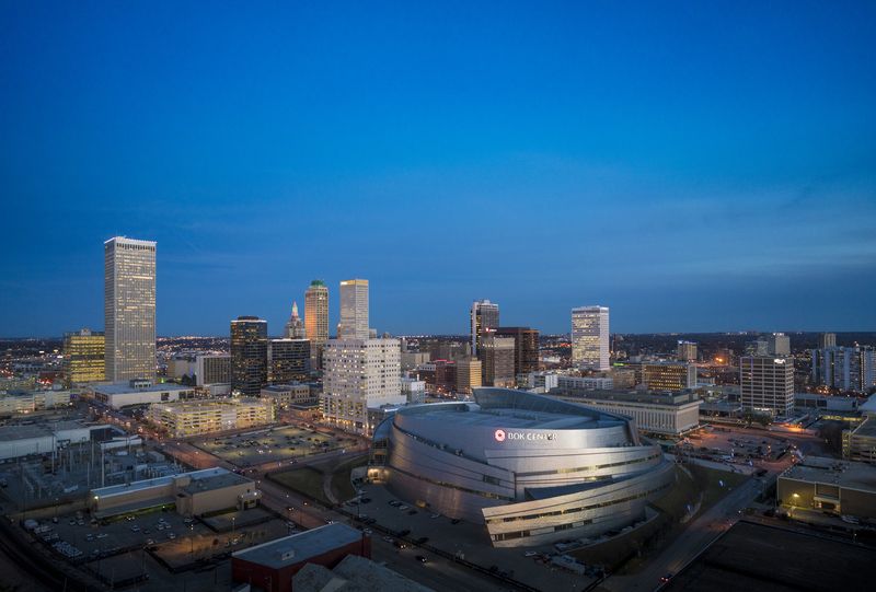 Luchtfoto van de skyline van Tulsa met kantoortorens en een moderne sportarena met gebogen dak, kort na zonsondergang