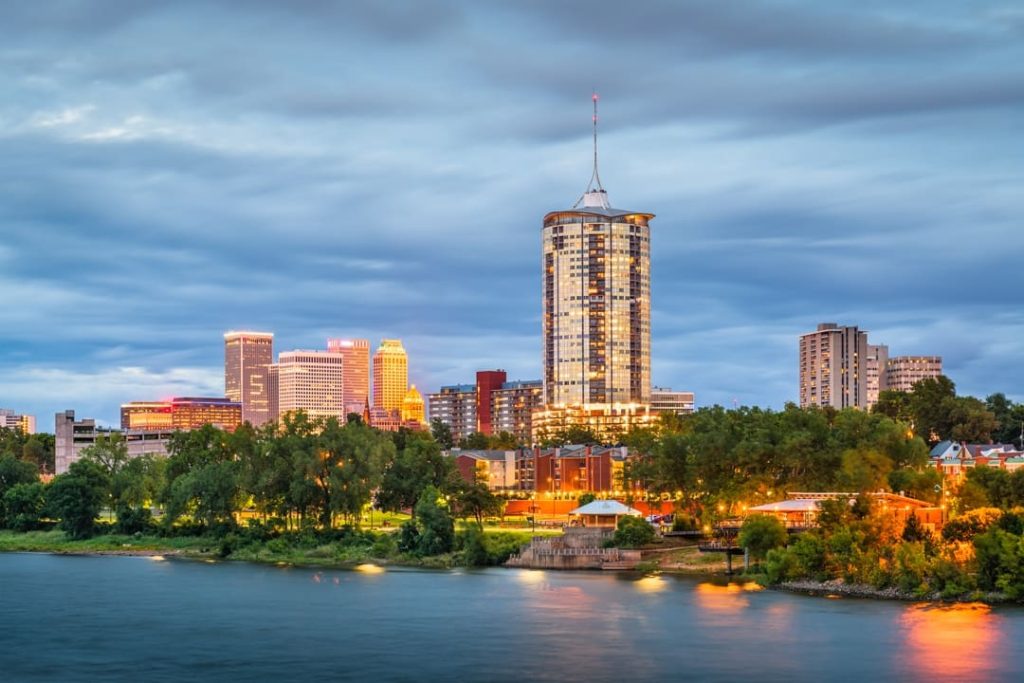 Skyline van Tulsa met een hoge ronde toren met puntdak, gezien over het water vanaf een park bij het vallen van de avond