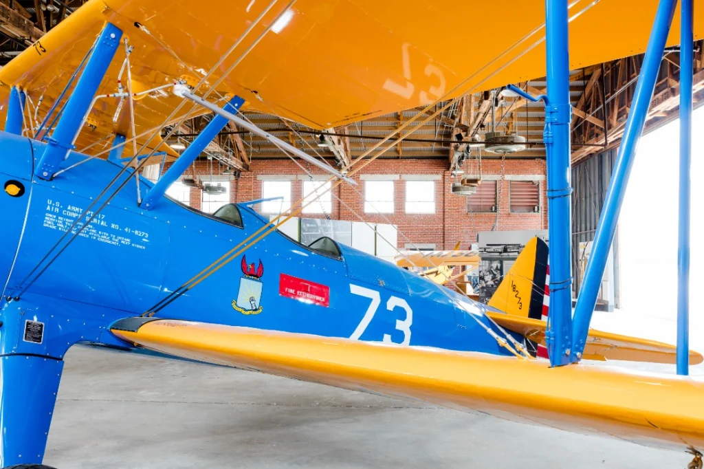 Een blauw met geel geschilderd historisch lesvliegtuig met het nummer 73 staat opgesteld in een hangar in Tuskegee