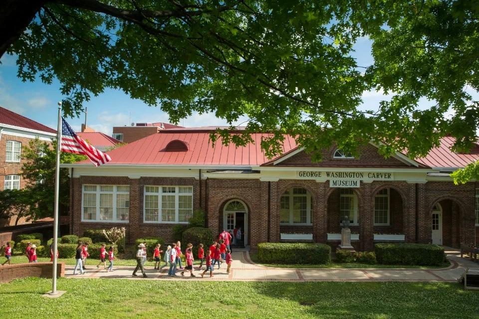 Groep schoolkinderen in rode kleding loopt voor het bakstenen George Washington Carver Museum in Tuskegee met Amerikaanse vlag