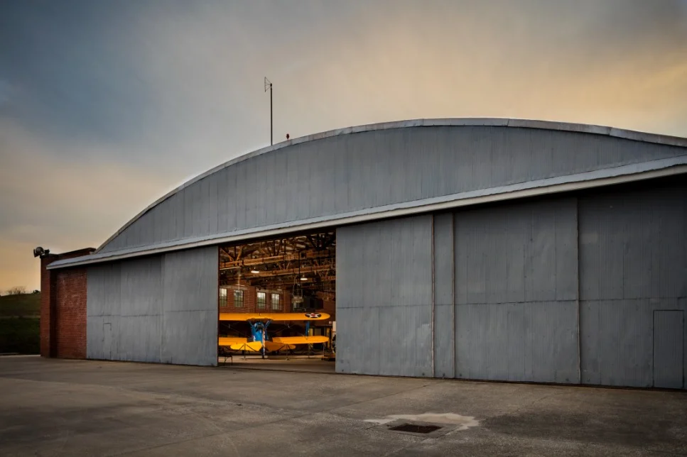 Een grote grijze hangar in Tuskegee met geopende schuifdeur waarachter een geel vliegtuig zichtbaar is bij avondlicht