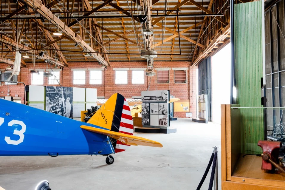 Blauw met geel gekleurd historisch vliegtuig met gestreepte staart staat opgesteld in een bakstenen hangar van het Tuskegee Airmen museum
