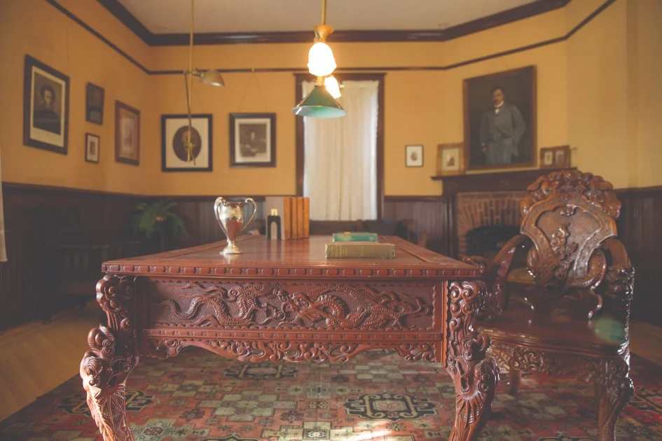 Interieur van een historische kamer in Tuskegee met een houten bureau vol houtsnijwerk, een open haard en ouderwetse portretten aan de muur