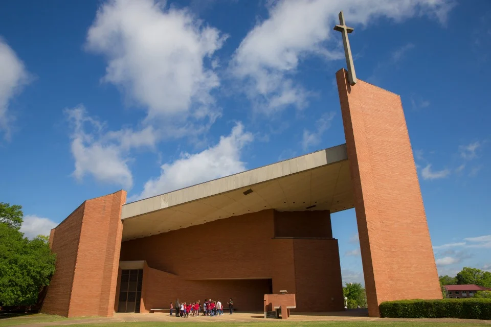 Moderne bakstenen kapel in Tuskegee met een hoog kruis en een groep bezoekers bij de ingang