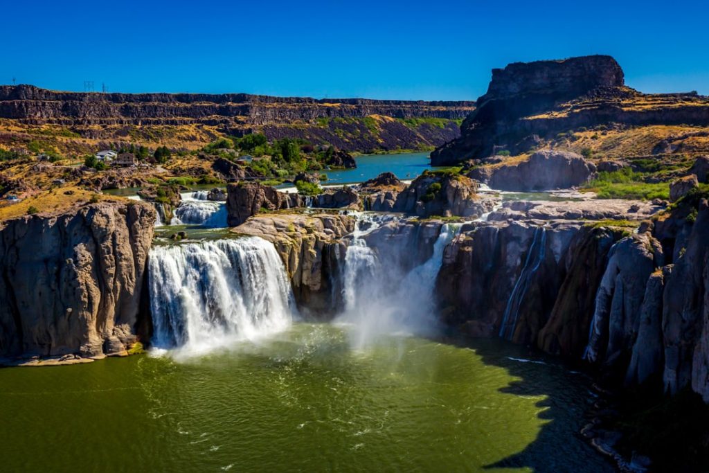 Brede waterval stort neer over rotsformaties in een groene kloof bij Twin Falls in Idaho onder een strakblauwe hemel