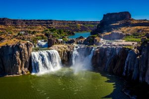 Brede waterval stort neer over rotsformaties in een groene kloof bij Twin Falls in Idaho onder een strakblauwe hemel