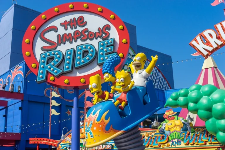 Kleurrijk attractiebord met de tekst The Simpsons Ride en figuren van de Simpsons familie in een achtbaanwagentje