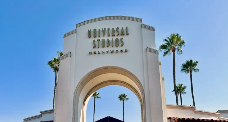 Close-up van de witte poortboog met het opschrift Universal Studios Hollywood omringd door palmbomen