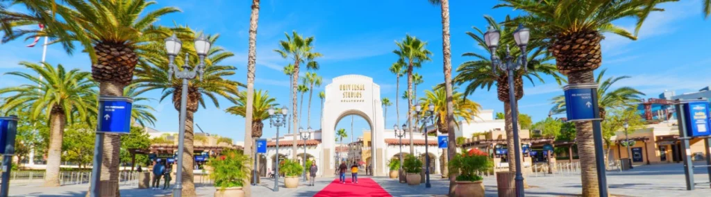Grote witte poortboog omzoomd door palmbomen met een rode loper naar de ingang van Universal Studios Hollywood