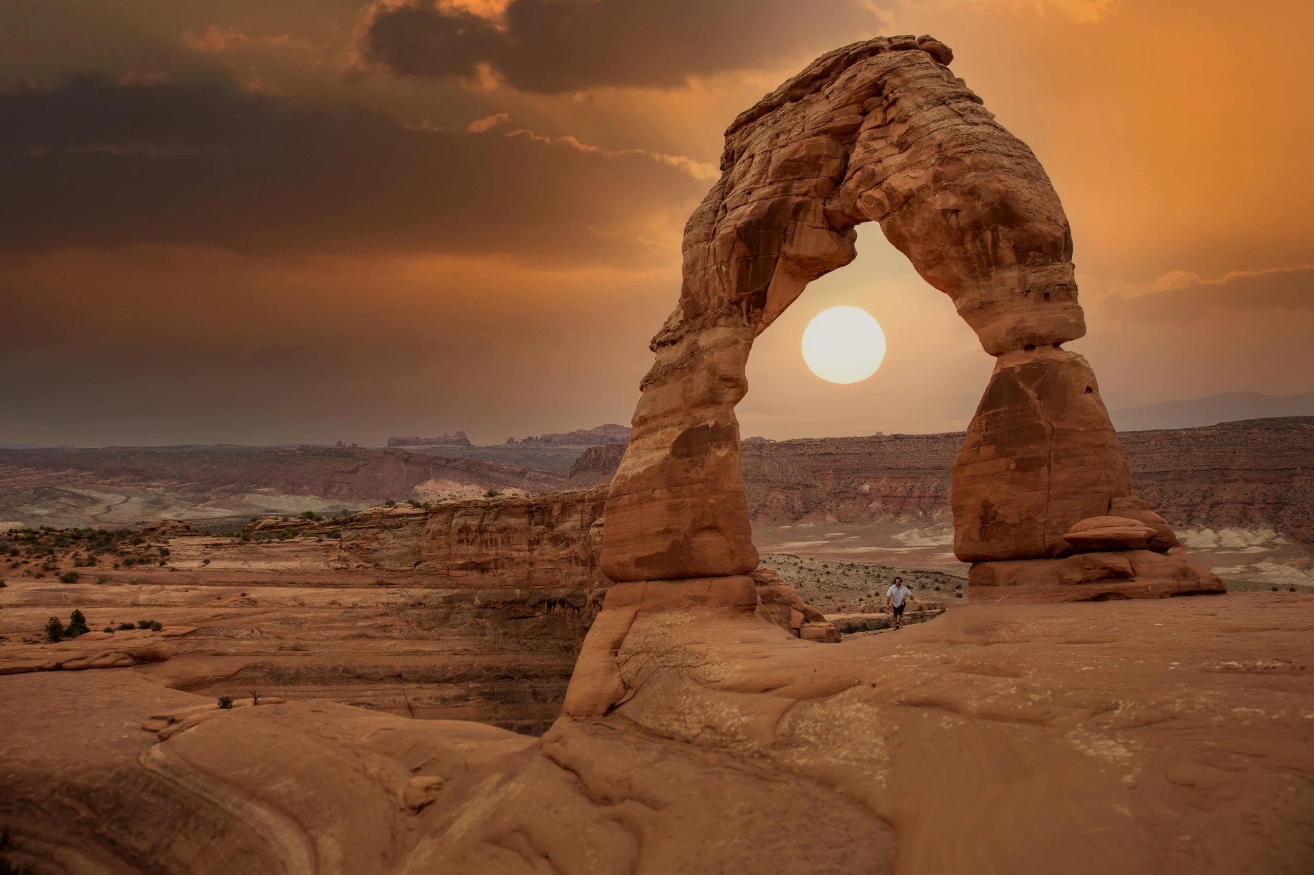 De zon zakt precies in de opening van de rotsboog Delicate Arch in Utah, terwijl een wandelaar bij de boog staat