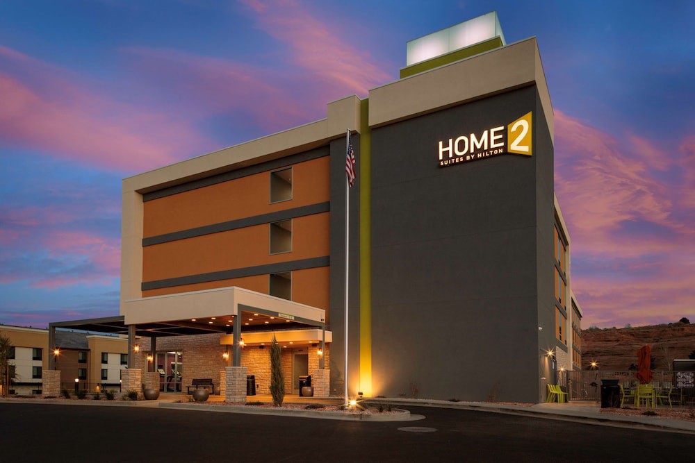 Modern hotelgebouw van Home2 Suites by Hilton met een overdekte oprit, verlicht tegen een roze en paarse avondlucht in Utah