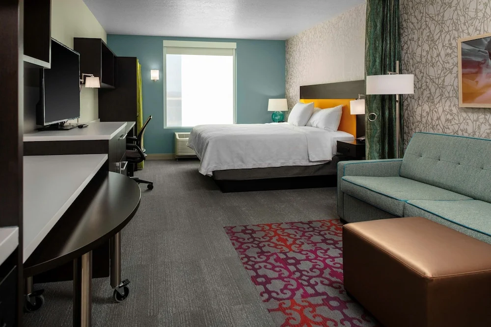 Hotelkamer met een tweepersoonsbed, televisie op een dressoir en een groene bank met een gordijn dat de kamer scheidt