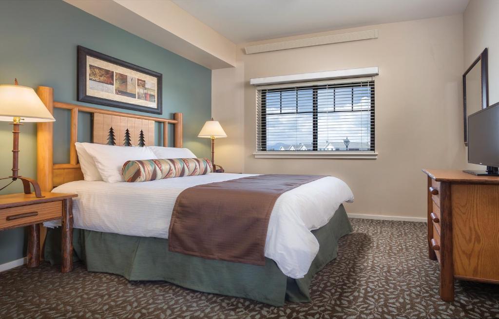 Hotelkamer met een tweepersoonsbed met houten hoofdbord met pijnboommotief, een blauwgroene fauteuil en een televisie