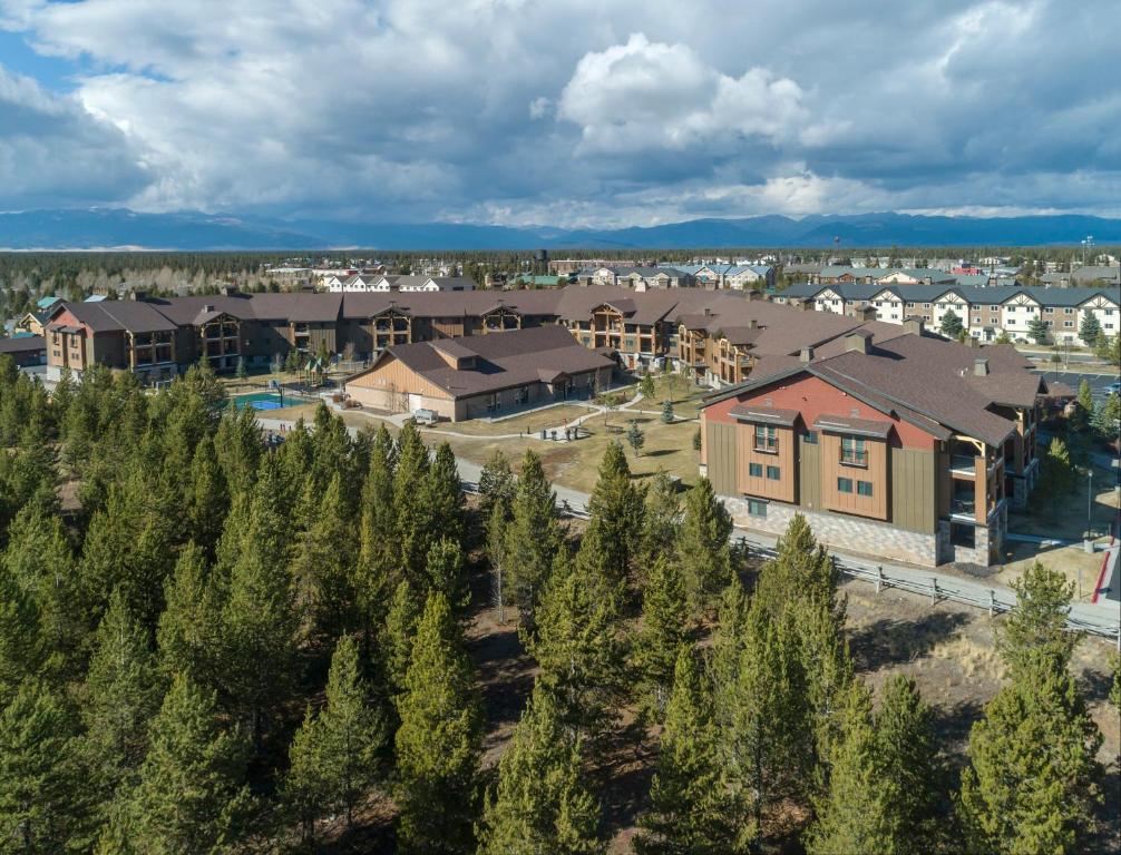 Luchtfoto van een vakantieresort met meerdere gebouwen tussen dennenbossen, met bergen en bewolkte lucht op de achtergrond