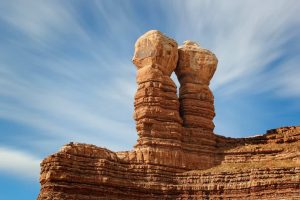 Twee smalle, gelaagde rotszuilen van zandsteen naast elkaar tegen een blauwe lucht met wolkenslierten in Utah