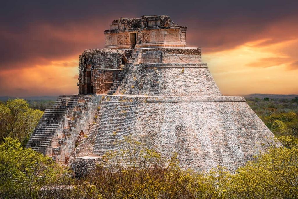 De ronde stenen Piramide van de Tovenaar steekt af tegen een oranje en paarse avondlucht in de ruïnestad Uxmal