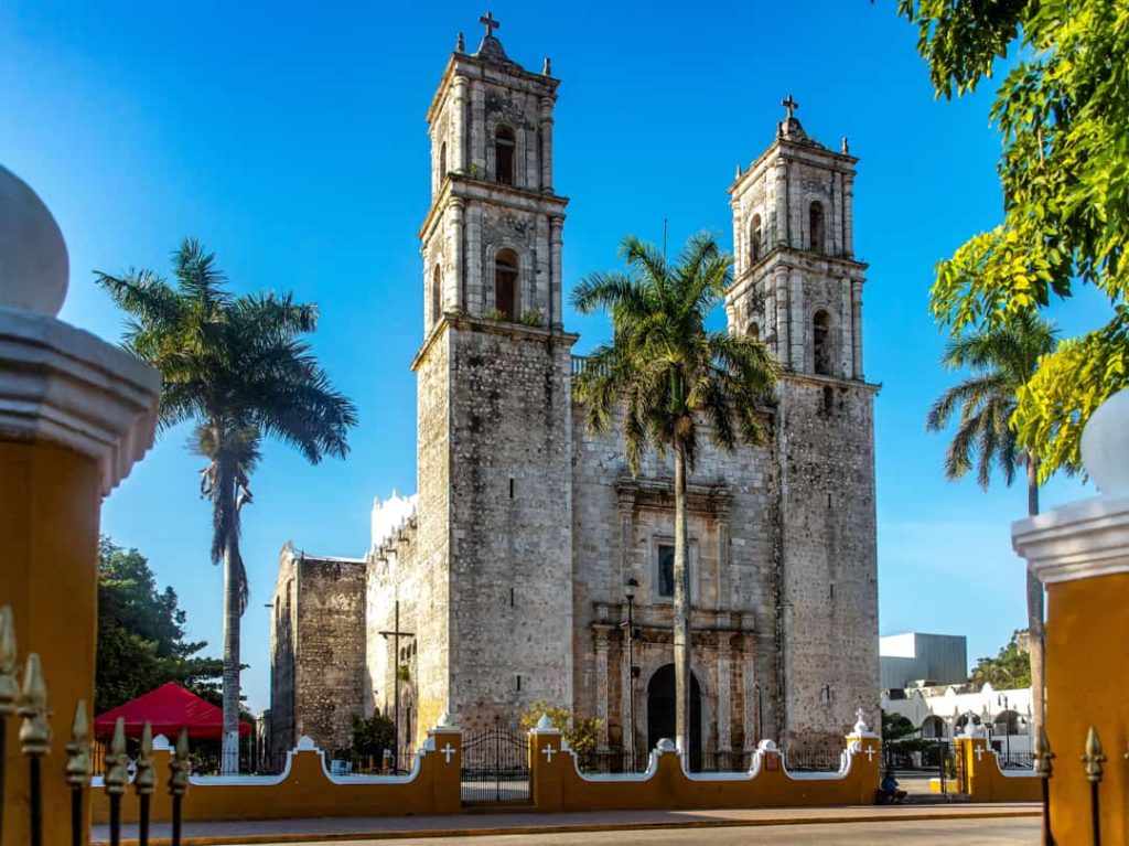 De stenen kathedraal San Servacio met twee torens en drie palmbomen ervoor onder een strakblauwe hemel in Valladolid