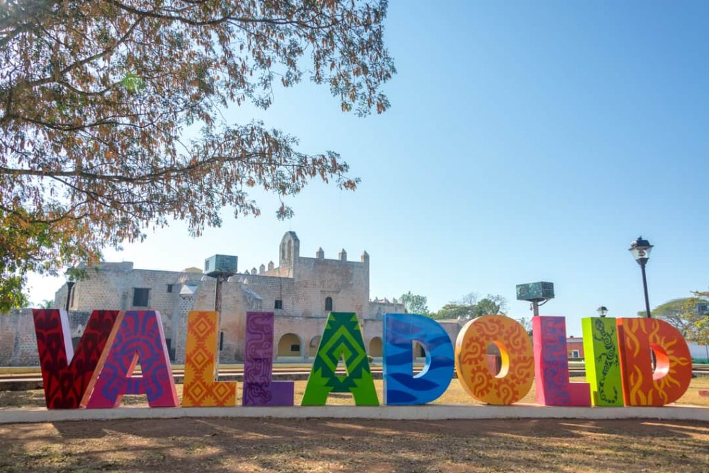 Grote kleurrijke letters vormen de naam Valladolid met op de achtergrond een wit koloniaal klooster