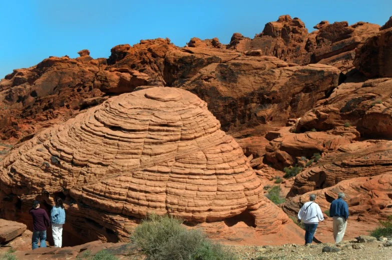 Kleine groep wandelaars staat naast een grote ronde, gestreepte rode zandsteenrots in Valley of Fire State Park bij Las Vegas