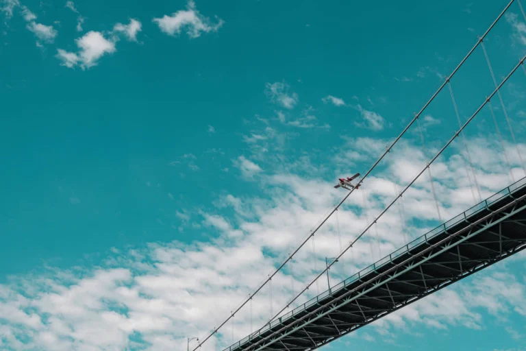 Een klein watervliegtuig vliegt door een blauwe wolkenlucht naast de kabels van een hangbrug in Vancouver