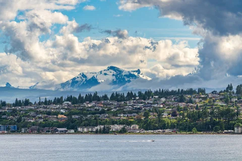 Uitzicht over het water op een kustplaats op Vancouver Island met besneeuwde bergtoppen en wolken op de achtergrond