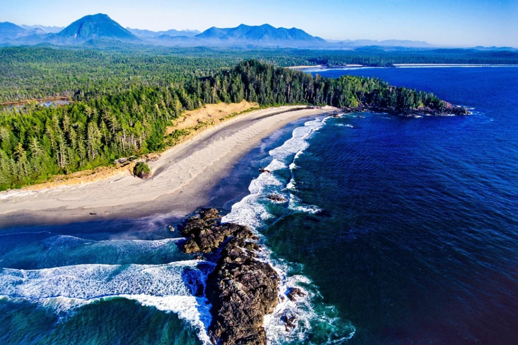 Luchtfoto van een afgelegen strand op Vancouver Island met dichte bossen, ruige rotsen en bergen op de achtergrond