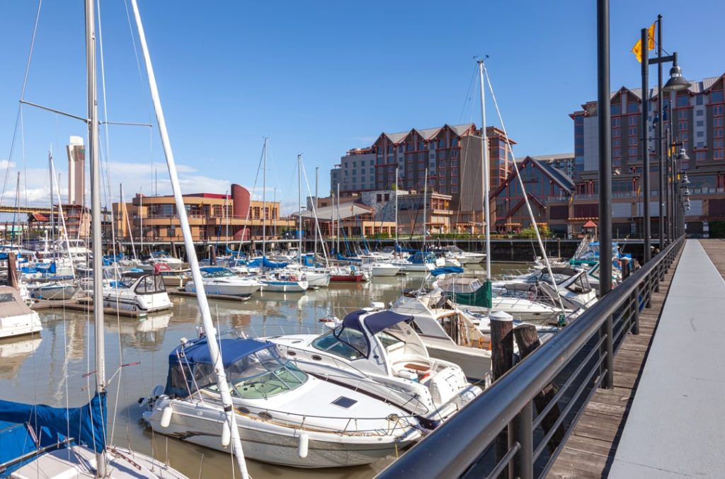 Zeilboten en een motorboot liggen afgemeerd in een jachthaven, met hotelgebouwen en een steiger met lantaarns op de achtergrond in Vancouver