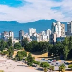 Luchtfoto van het strand en de wolkenkrabbers van Vancouver met besneeuwde bergen en de zee op de achtergrond