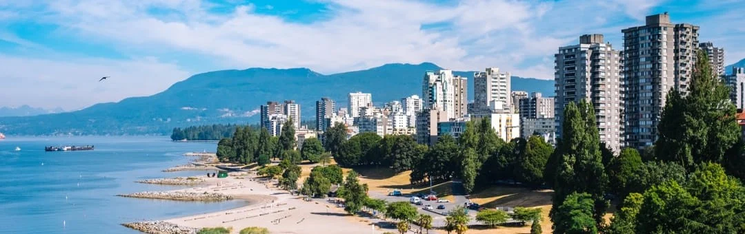 Luchtfoto van het strand en de wolkenkrabbers van Vancouver met besneeuwde bergen en de zee op de achtergrond