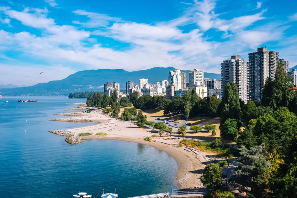Luchtfoto van een zandstrand langs English Bay met wolkenkrabbers, groene bomen en bergen op de achtergrond in Vancouver