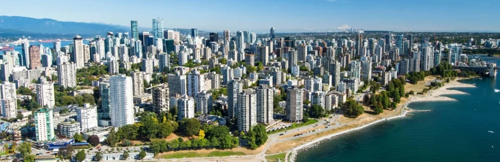 Luchtfoto van hoge woontorens in het West End van Vancouver naast een strand aan de baai, met bergen op de achtergrond