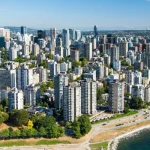 Luchtfoto van hoge woontorens in het West End van Vancouver naast een strand aan de baai, met bergen op de achtergrond