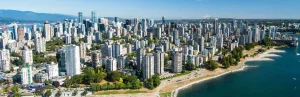 Luchtfoto van hoge woontorens in het West End van Vancouver naast een strand aan de baai, met bergen op de achtergrond