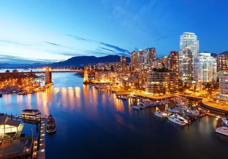 Verlichte wolkenkrabbers en een brug weerspiegelen in het water van de jachthaven in Vancouver tijdens de schemering